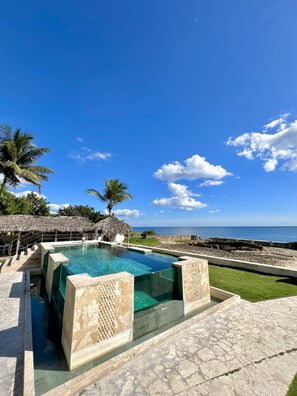 Relax by the pool surrounded by a deck and a low wall, with a glass viewing section offering a glimpse of the ocean.