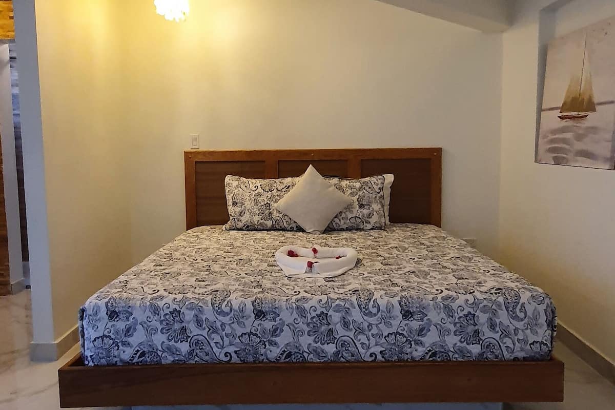 Une chambre à coucher avec un lit, une table de chevet, une lampe fixée au mur et un tableau.