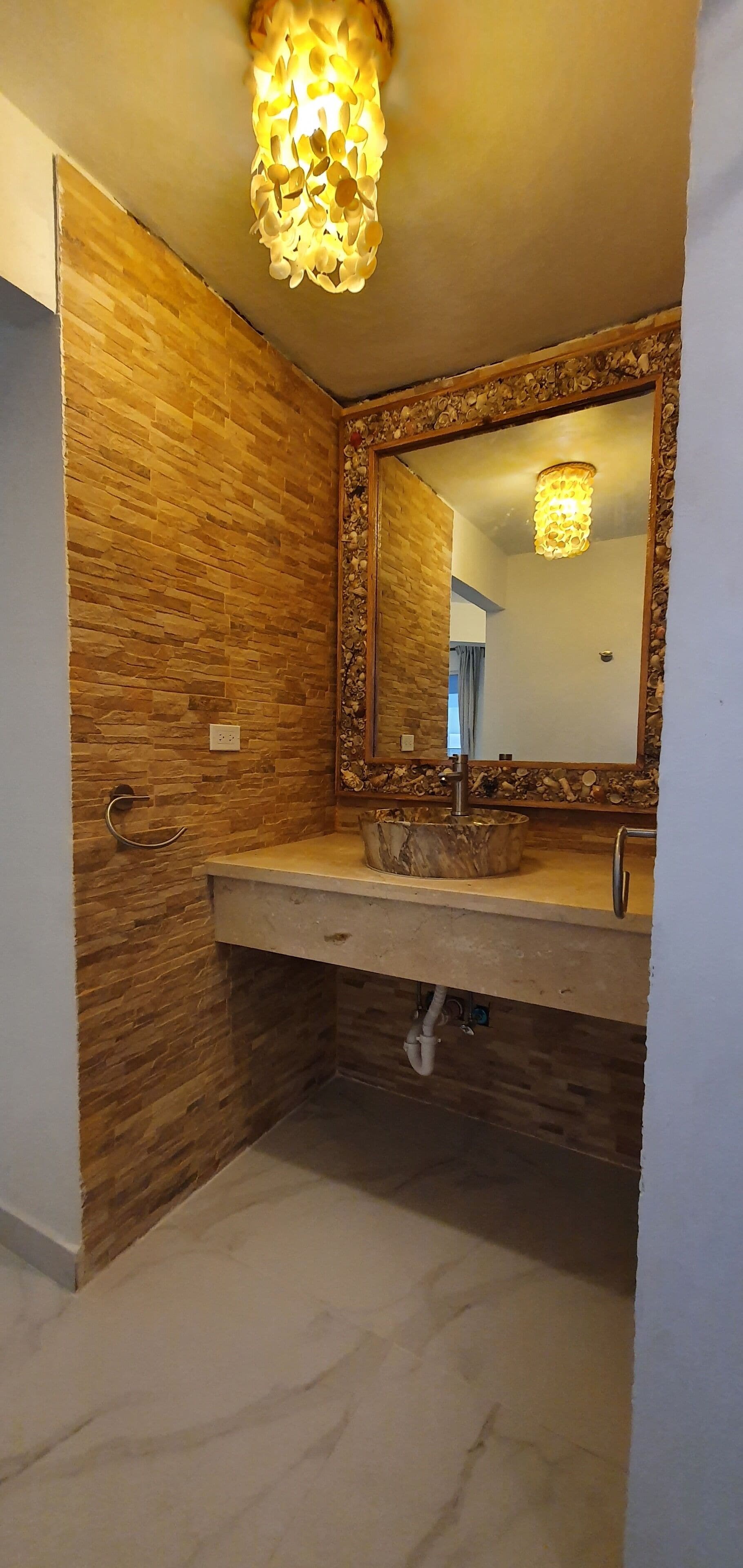 Ein Badezimmer mit einer Holzwand, einem Waschbecken mit Natursteinbecken und einem Spiegel mit dekorativem Rahmen.