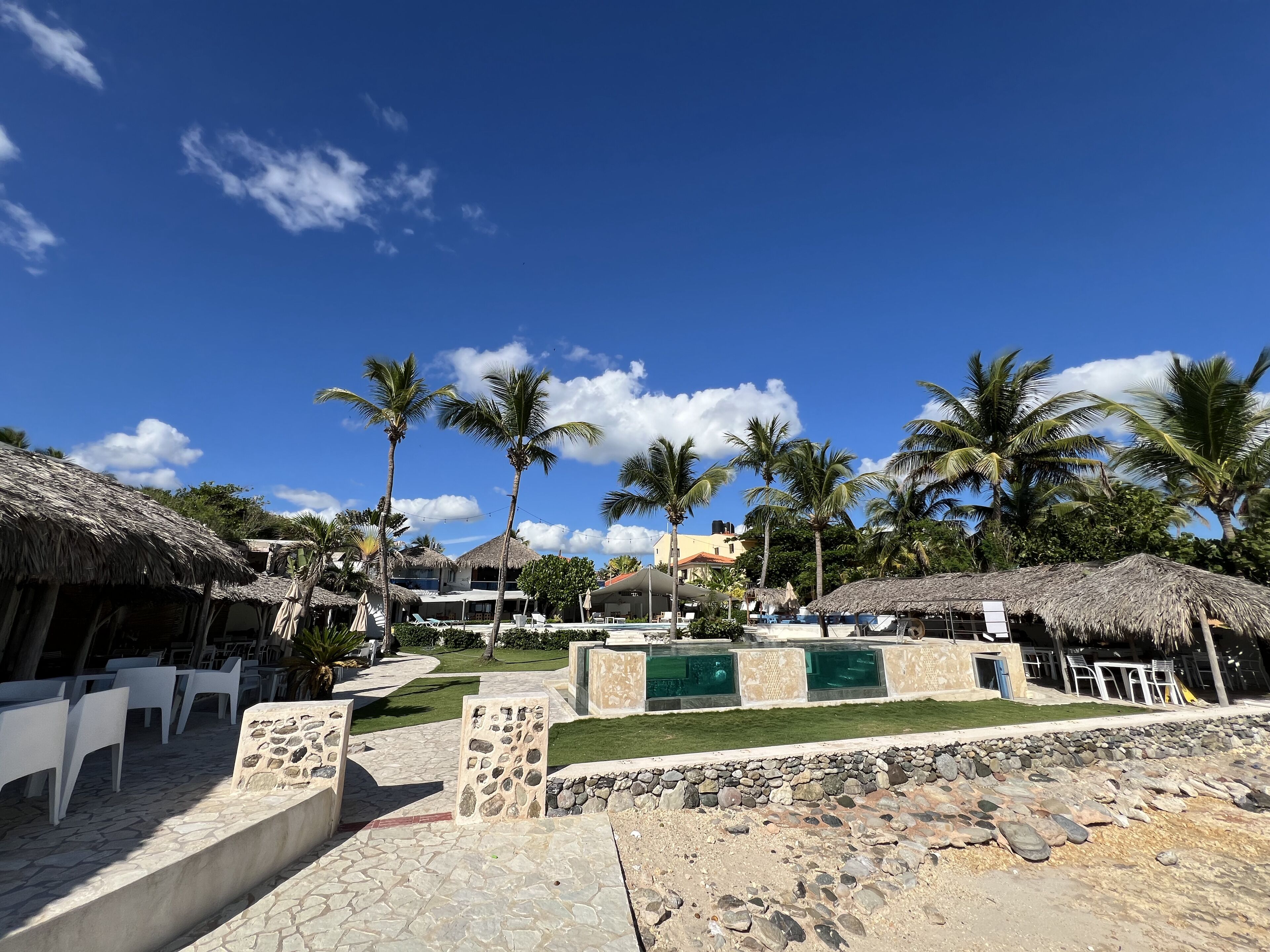 A resort with thatched-roof huts, palm trees, and outdoor seating areas.
