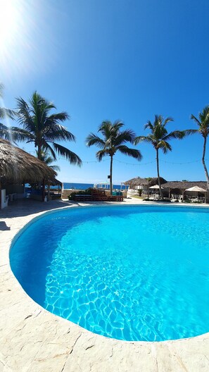 Relax by the serene pool surrounded by a sandy beach and palm trees.