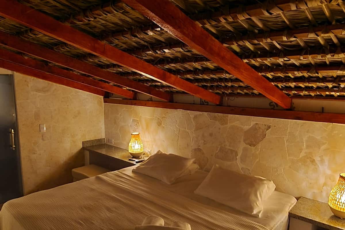 Une chambre à coucher avec un lit, une table de chevet, une lampe et un mur en pierre.