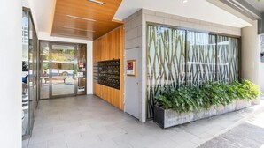 A modern building entrance with a glass door, wooden panel wall, and a planter with green plants.
