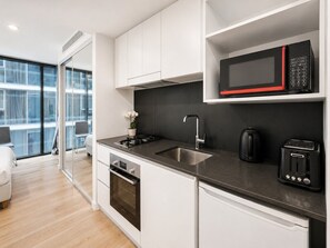 A modern kitchen with white cabinets, a black countertop, a microwave, a toaster, and a sink. - Stylish Studio on High Level-Close to Brisbane CBD (South Brisbane)