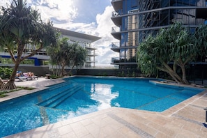 A swimming pool with steps leading into it, surrounded by palm trees and a modern building with balconies.