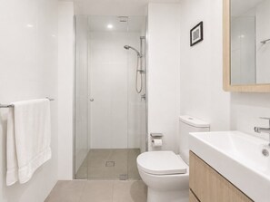 Un baño moderno con ducha envuelta en vidrio, inodoro blanco y tocador de madera con espejo.