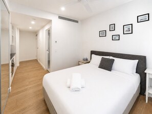 A hotel room with a large bed, a bedside table, a nightstand, and a wall with framed pictures. - Stylish Studio on High Level-Close to Brisbane CBD (South Brisbane)