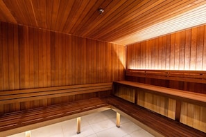 A sauna with wooden walls and benches, a tiled floor, and a ceiling light.