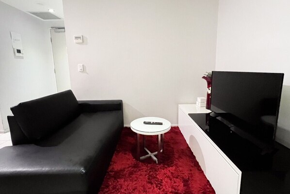 A modern living room with a black leather sofa, a small white round table, a flat-screen TV, and a red carpet.