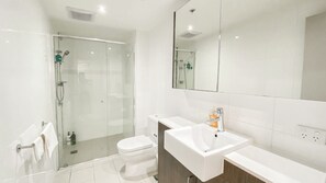 A modern bathroom with a glass-enclosed shower, a white toilet, and a white sink with a mirror above. - Discover Urban:1BR|Pool|Gym|Sauna|Convenient (Brisbane City)