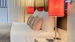 A modern hotel room with a bed, two bedside lamps, a painting, and a window with curtains. - Discover Urban:1BR|Pool|Gym|Sauna|Convenient (Brisbane City)