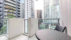 A balcony with a wicker table and chair, a glass door, and a view of high-rise buildings. - Discover Urban:1BR|Pool|Gym|Sauna|Convenient (Brisbane City)