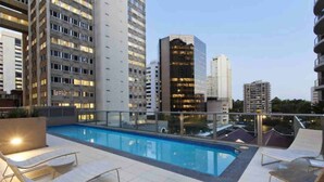 A rooftop pool area with a glass balustrade, lounge chairs, and a view of surrounding high-rise buildings. - Discover Urban:1BR|Pool|Gym|Sauna|Convenient (Brisbane City)