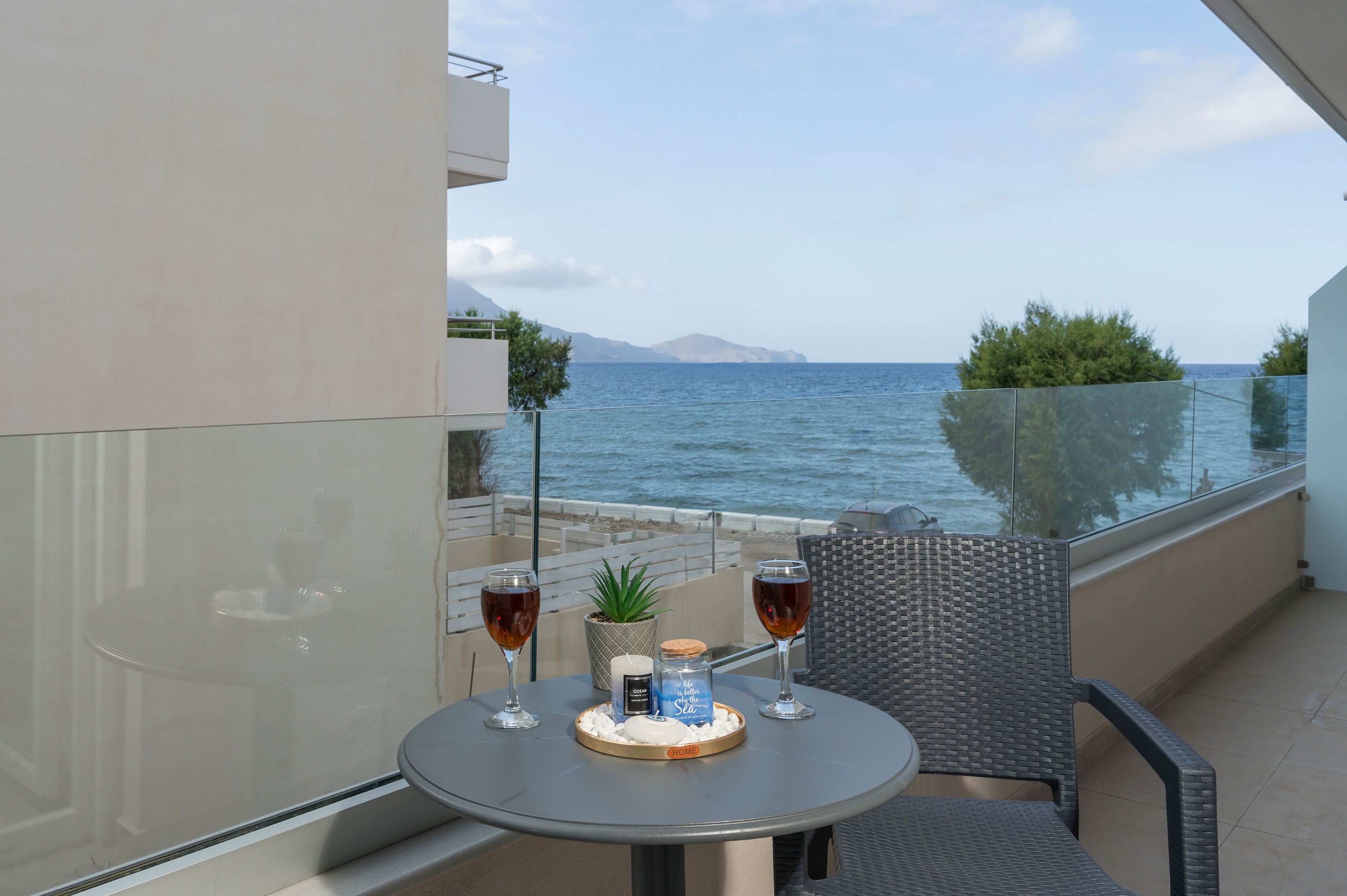 A balcony with a table, two glasses of red wine, a candle, and a small plant.