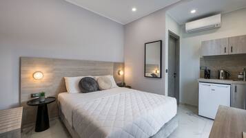 Quarto de hotel moderno com cama grande, mesas de cabeceira, pequena área de cozinha e ar condicionado.