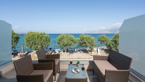 A balcony with wicker furniture, a table with a tray and glasses, and a view of the sea and trees. - Alexia Seaview Apartments  (Kissamos)