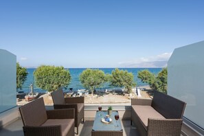 Enjoy a refreshing drink on the balcony with a view of the sea, surrounded by wicker furniture and lush greenery.