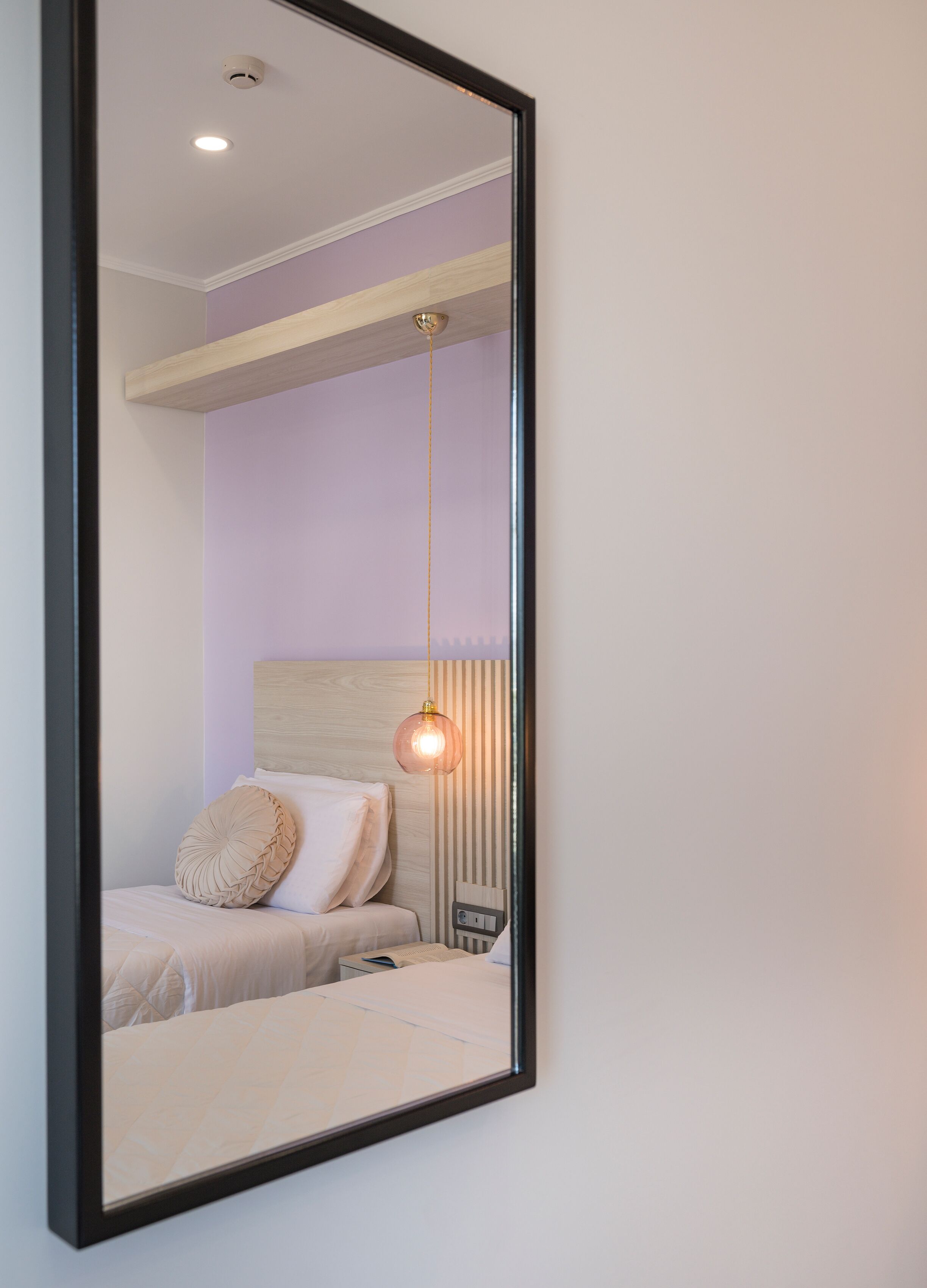 A bedroom with a bed, a nightstand, a mirror, and a hanging light fixture.