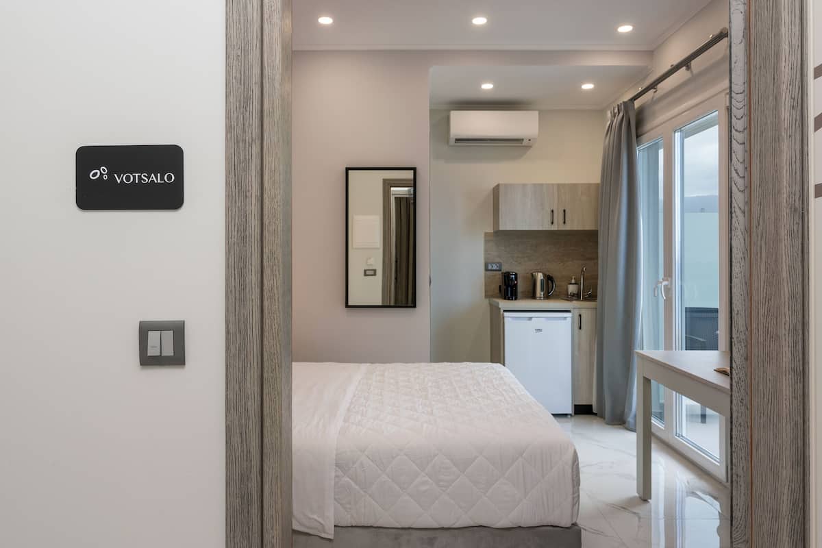 A modern hotel room with a bed, a small kitchenette, and a view of the city.