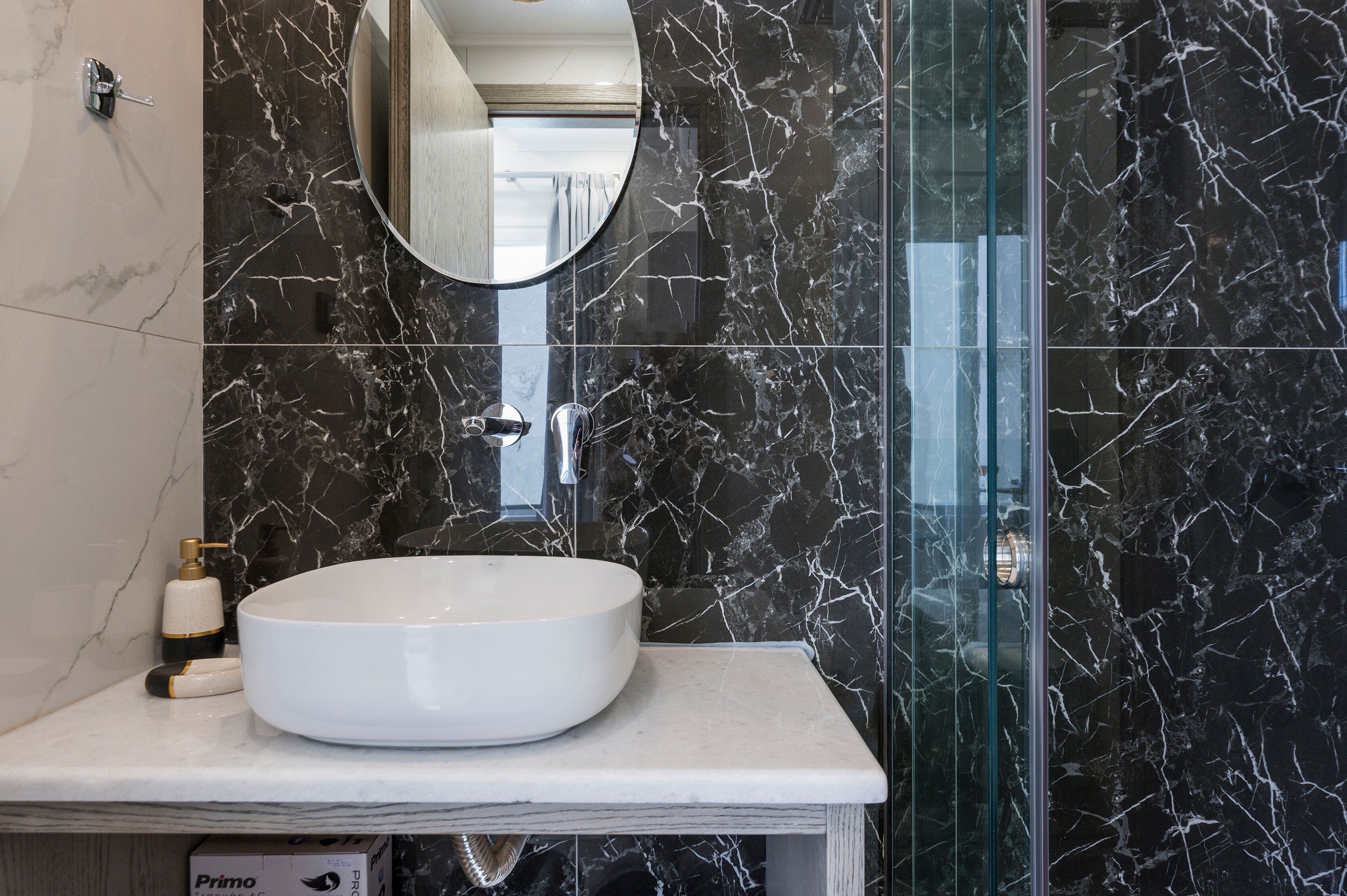 Une salle de bain avec un lavabo blanc, un miroir et des murs en marbre noir.