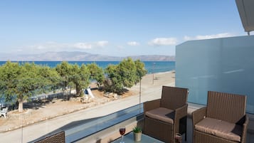 A balcony with wicker furniture, a glass table, and a view of the sea and mountains.