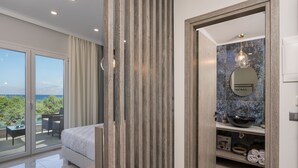 A modern bedroom with a large bed, a balcony with a table and chairs, and a bathroom with a sink and mirror. - Alexia Seaview Apartments (Kissamos)