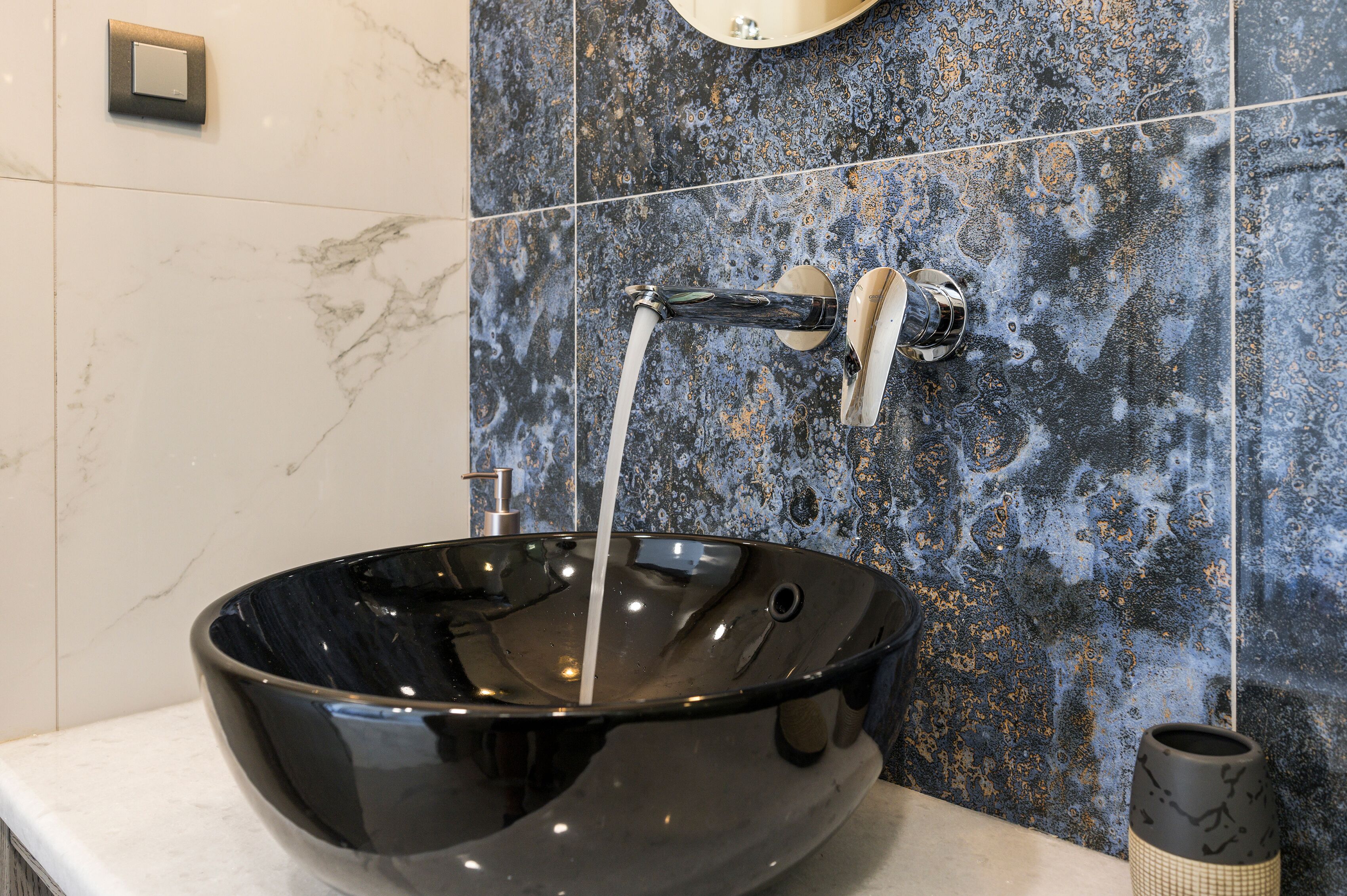Un baño moderno con un lavamanos tipo cuenco negro, un grifo y un salpicadero de mármol.