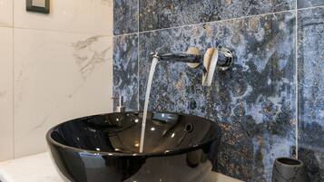 Un baño moderno con un lavamanos tipo cuenco negro, un grifo y un salpicadero de mármol.