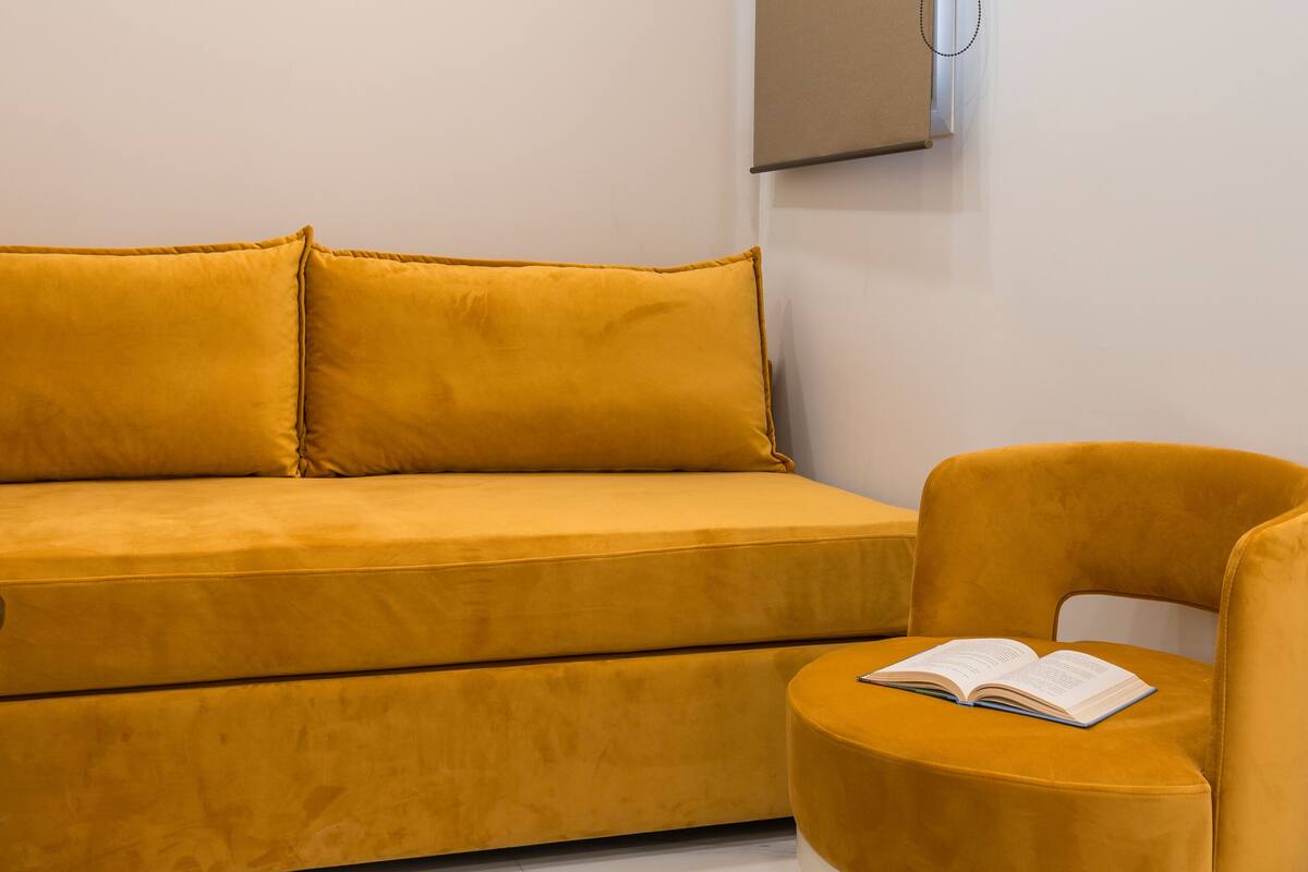 A yellow sofa and chair in a room with a white wall and a mounted television.