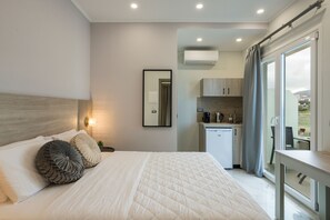Relax in a serene space with a large bed, bedside table, and bench, plus a compact kitchenette and balcony.