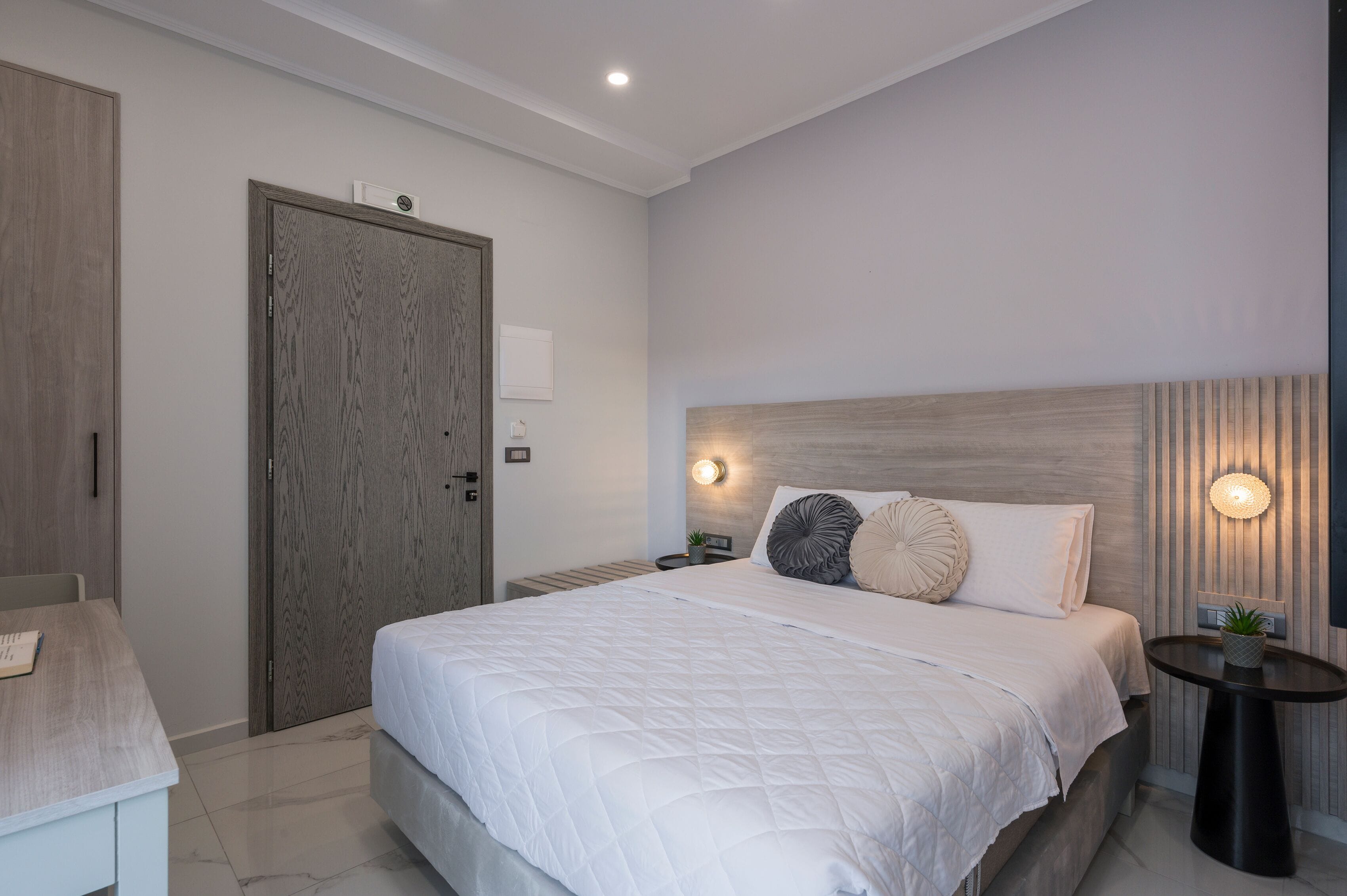 A modern bedroom with a large bed, bedside tables, a wooden wardrobe, and a wall-mounted light fixture.