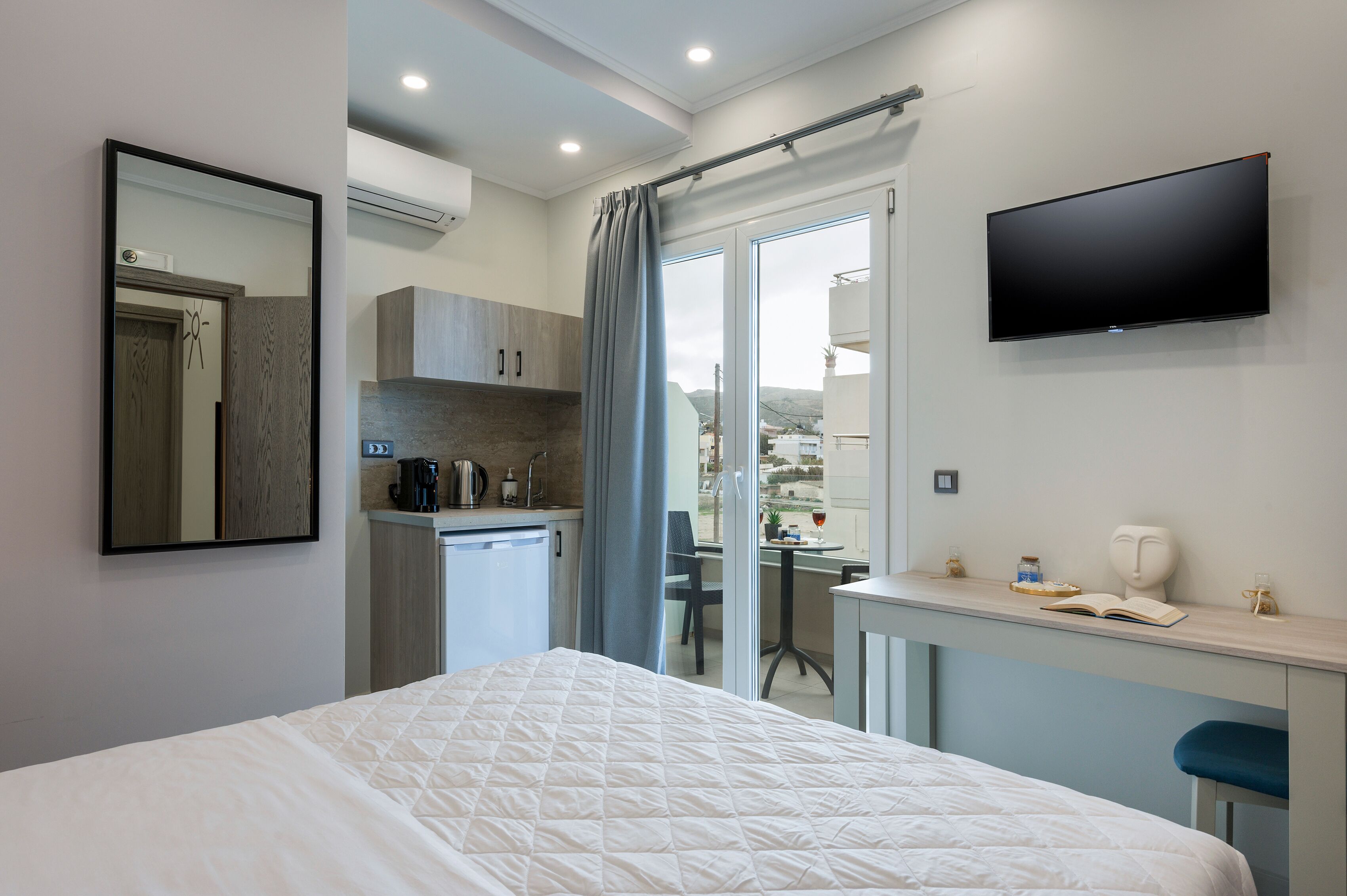 Una camera d'albergo con un letto, una scrivania con una sedia, una televisione, un angolo cottura e una porta scorrevole in vetro che dà sull'esterno.