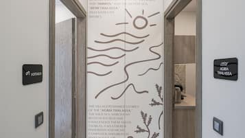 A hallway with a decorative wall panel featuring a sun and waves, and signs for 'VOTSALO' and 'AGRIA THALASSA'.