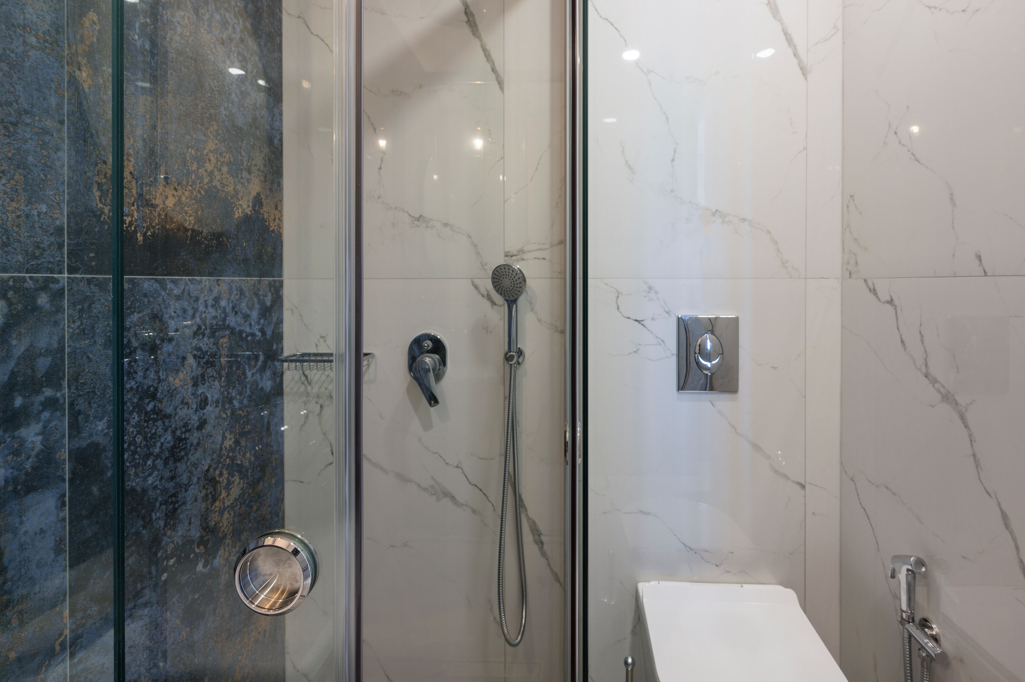 Un bagno moderno con doccia vetrata, lavandino bianco e pareti in marmo.