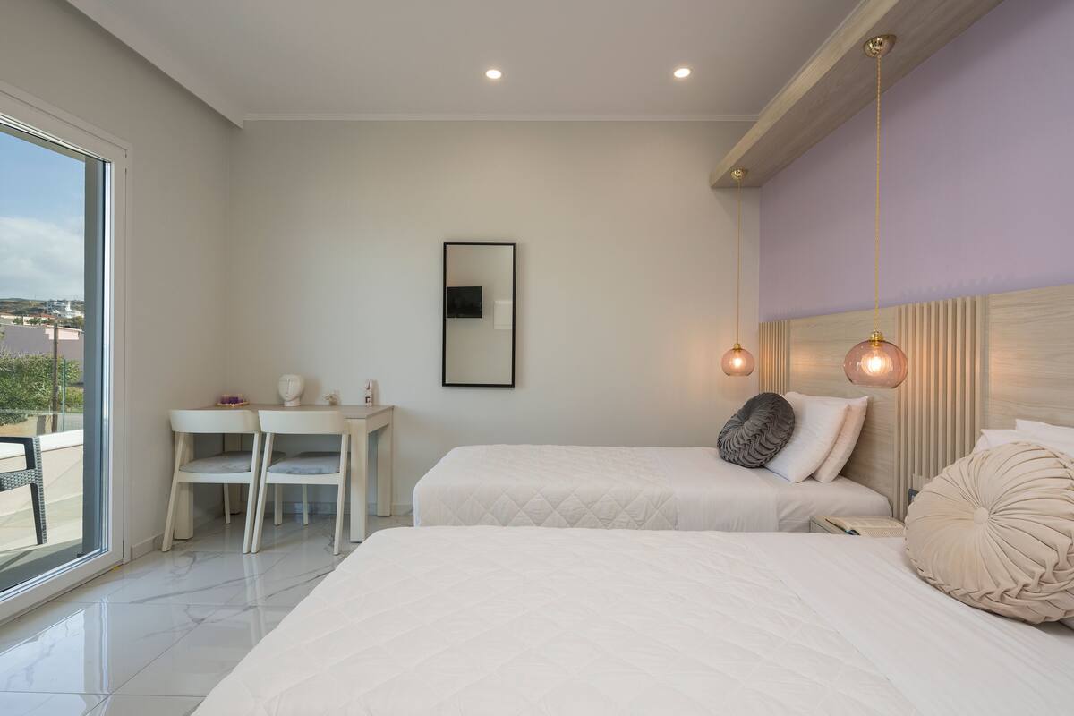 A modern bedroom with two beds, a desk, and a large window.