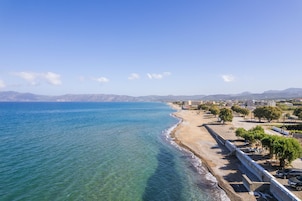 A coastal view with a beach, clear blue sea, and distant mountains.