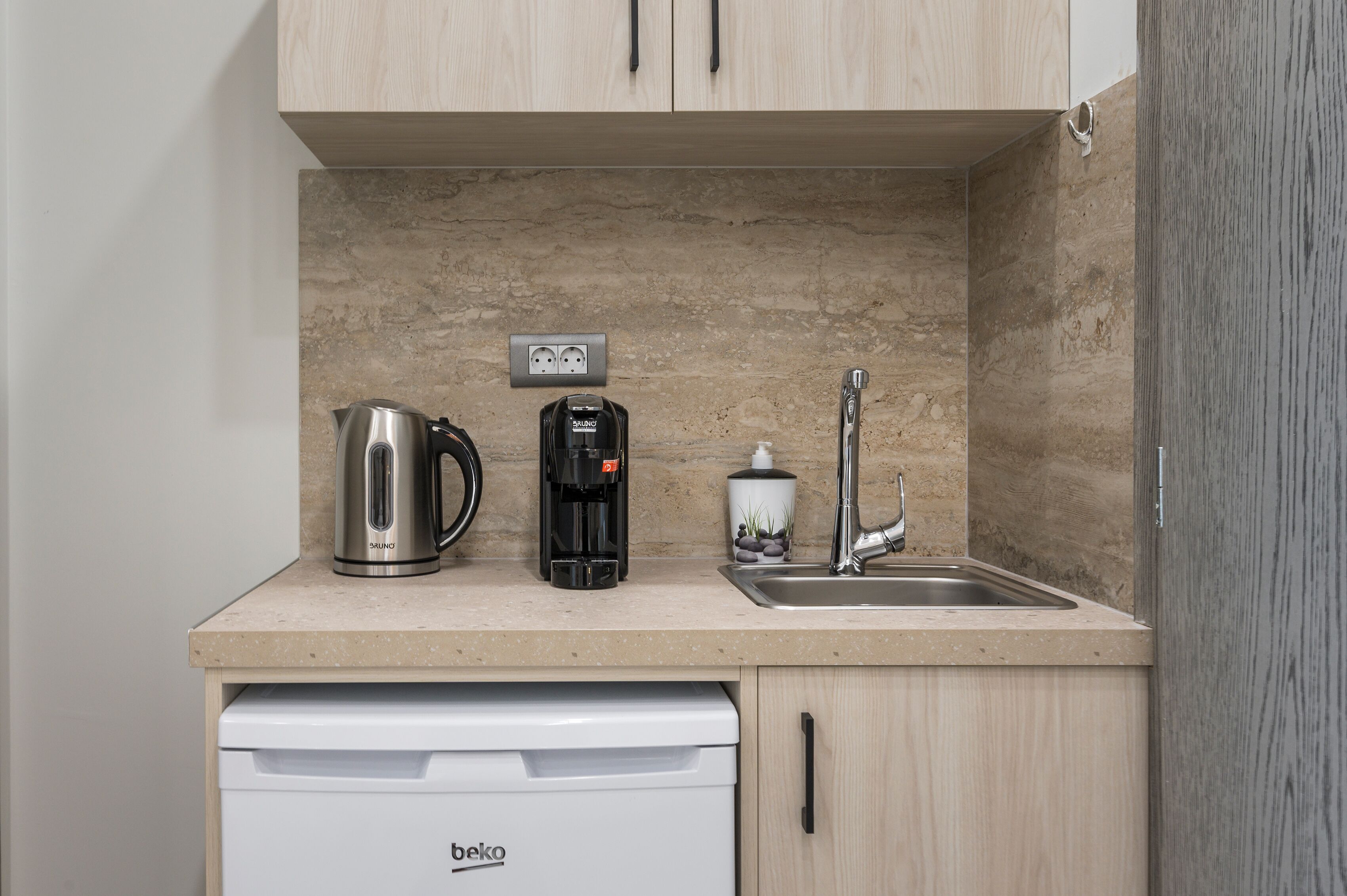 A kitchenette with a coffee maker, a kettle, a sink, and a dishwasher.