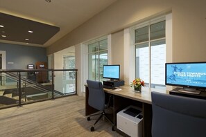 Un espace de bureau moderne équipé de deux écrans d’ordinateur, d’une imprimante et d’une rambarde en verre donnant sur un escalier.
