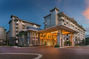 A multi-story hotel with a covered entrance, outdoor seating area, and a landscaped courtyard. - Hilton Head Island | Oceanfront Family Stay | Pool + Beach | 2BR (Hilton Head Island)