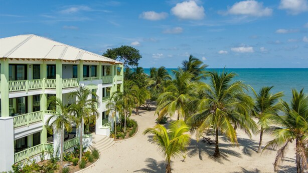 A resort with a beach view, multiple floors, and palm trees. - Beach Walkout Condo 112 3BR/2BA Sleeps 8 (Placencia)