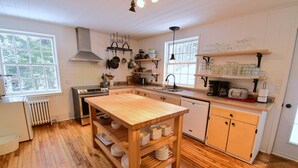 A kitchen with wooden floors, a central island, a stove, a sink, and various kitchen utensils and appliances. - Le Partage Lodge (Val Morin)