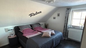 Ein Schlafzimmer mit einem Bett, einem Nachttisch, Vorhängen an einem Fenster und einer Wandleuchte.