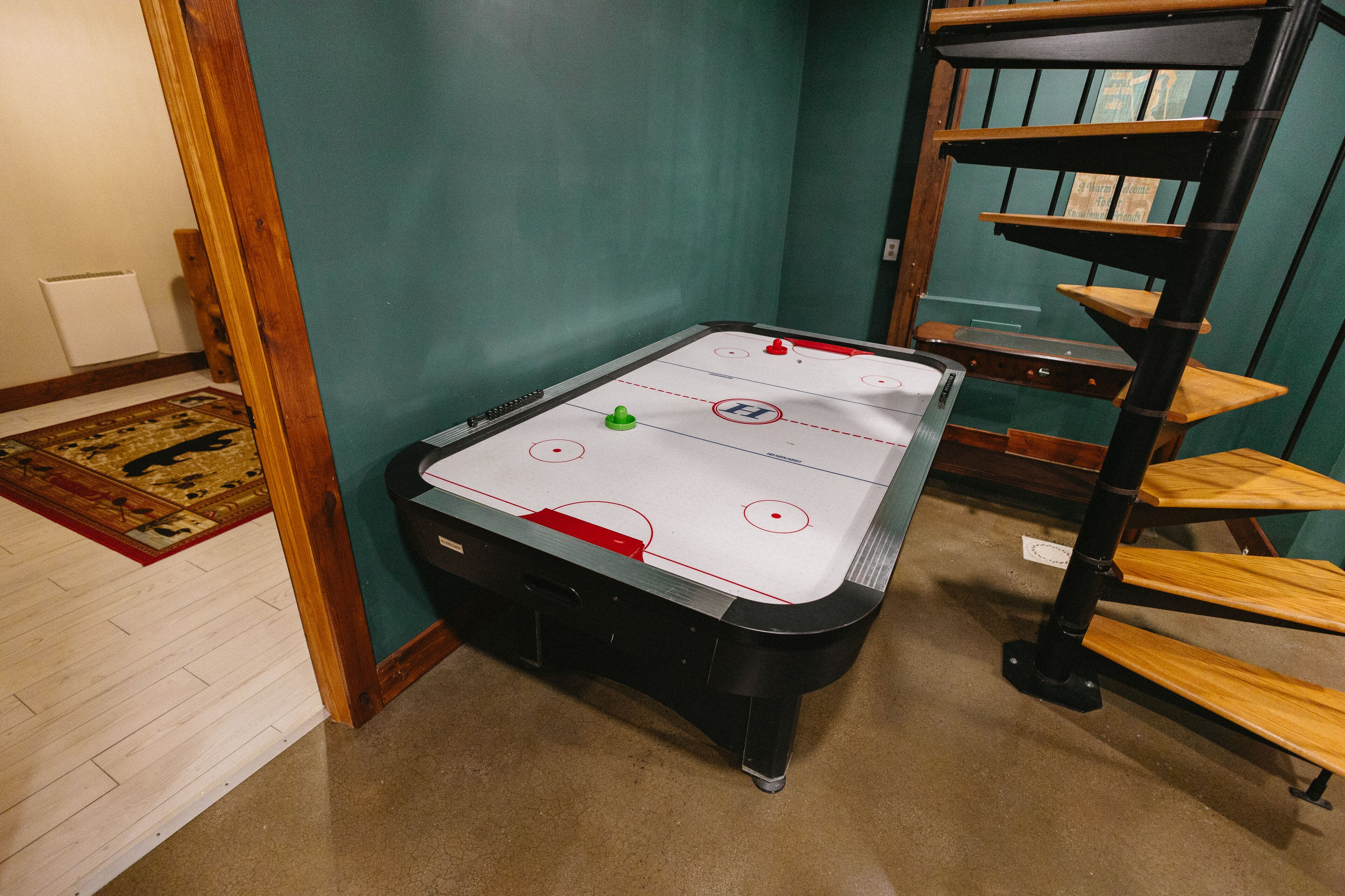 A room with a hockey table, a wooden bench, and a green wall.