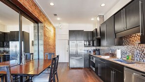 Una cocina moderna con armarios oscuros, electrodomésticos de acero inoxidable y una mesa de comedor de madera.