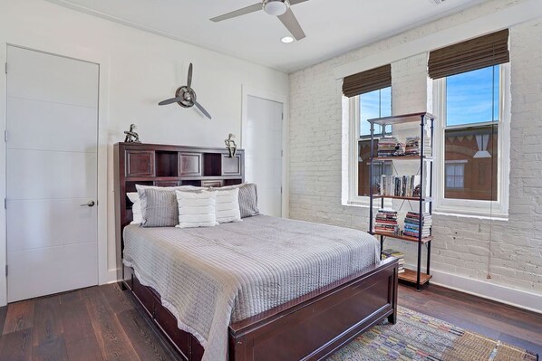 A bedroom with a wooden bed, a bookshelf, and a large window with blinds.