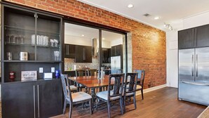 Una cocina moderna con pared de ladrillo, electrodomésticos de acero inoxidable y un comedor con sillas y mesa de madera.