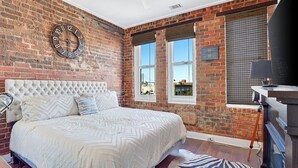 Un dormitorio con pared de ladrillo, cama grande, ventilador de techo y vistas al exterior.