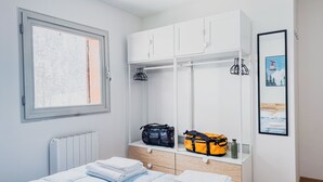 Et soveværelse med seng, garderobeskab, radiator, et vindue med udsigt og et billede i ramme på væggen.