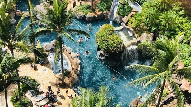A resort pool area with multiple water features, palm trees, and lounge chairs. - Waikiki | Lagoon Resort | Pools & Beach | 2BR Plus (Honolulu Oahu)