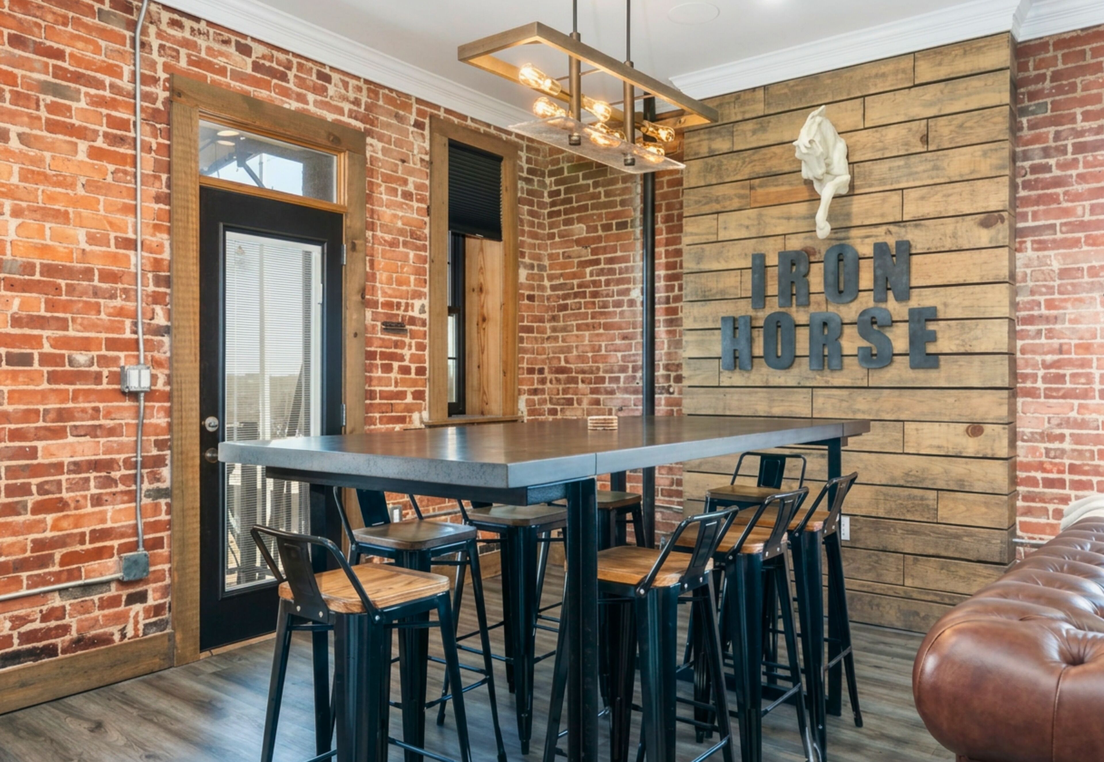 Un comedor con pared de ladrillo, un letrero de madera que dice 'IRON HORSE' y una lámpara moderna.
